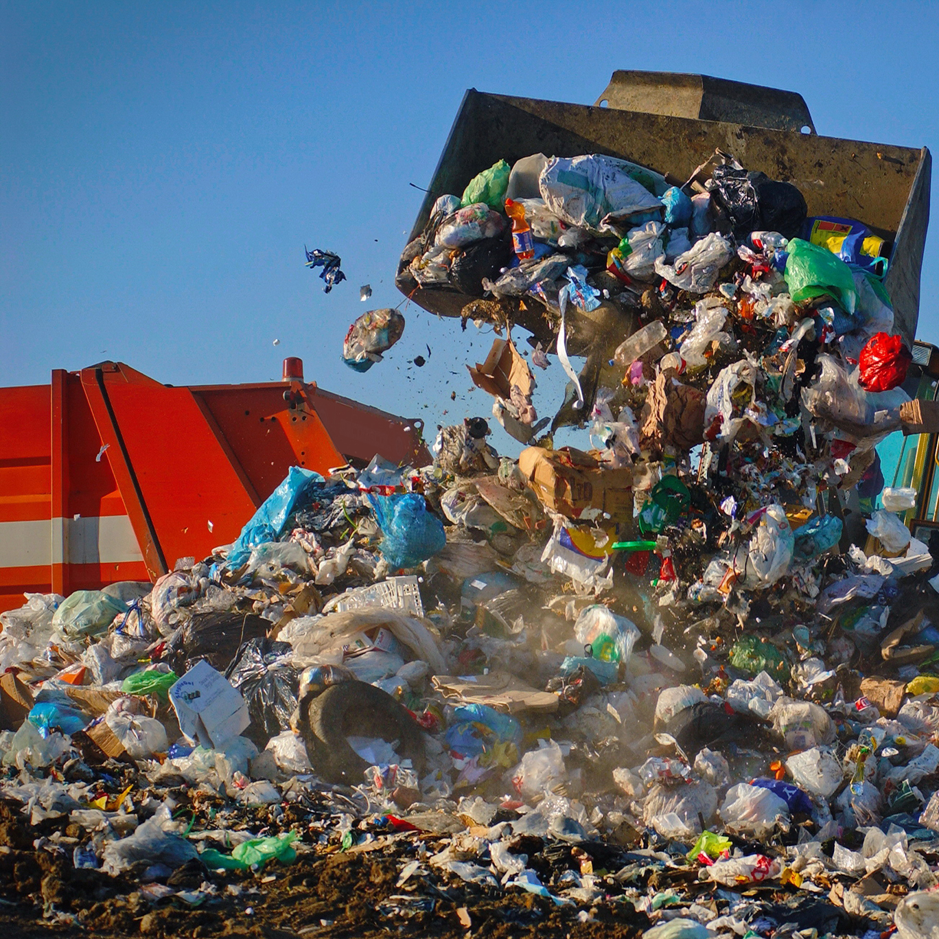Garbage Truck dumping trash in a landfill and a machine moving trash around.