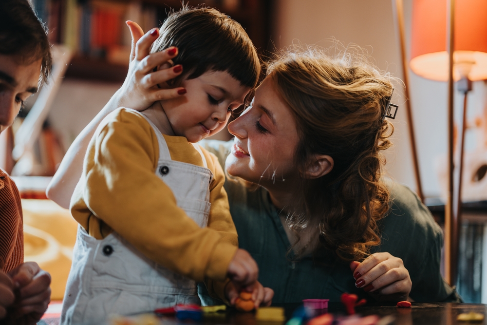 mom smooching young son who is playing with blocks